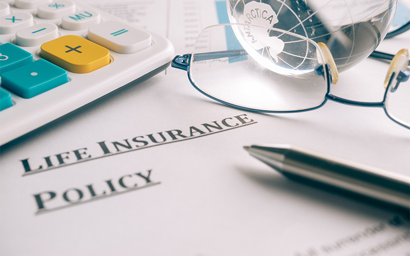 A life insurance policy document on a desk with a calculator, pen, eyeglasses, and a globe, symbolizing financial planning and insurance coverage.