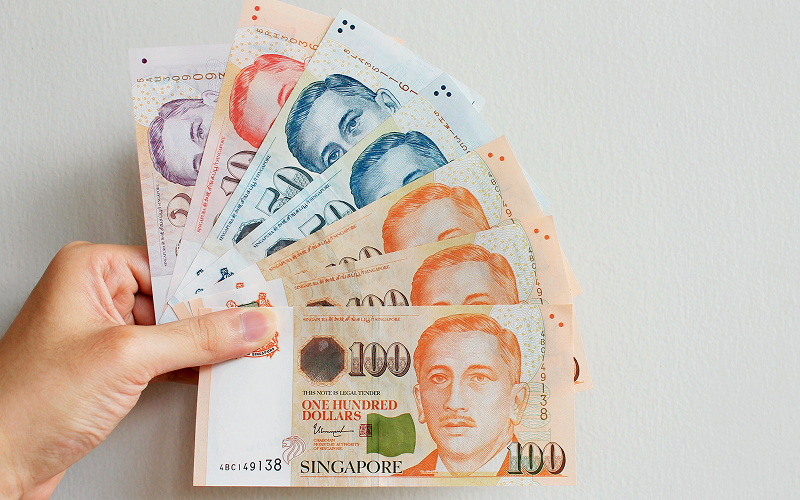 Hand holding Singapore dollar notes for immediate policy cash access.